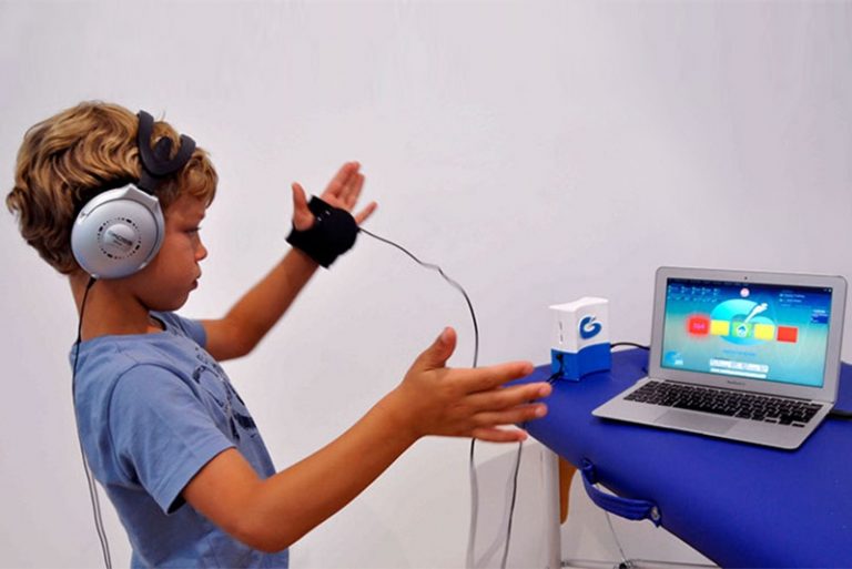 Boy wearing headphones controls laptop with hand gestures.